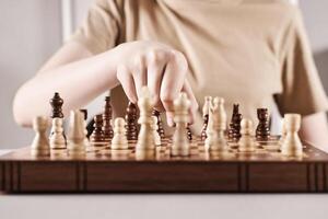 Hand holds chess piece and makes a move. Faceless boy develops game strategy, selective focus on hand photo