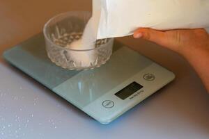 Weighing sugar from a pack on a kitchen scale on the kitchen table photo