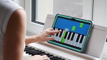 Hands playing a keyboard while following an interactive learning app on a tablet. Technology enables self-education in music without traditional lessons. video