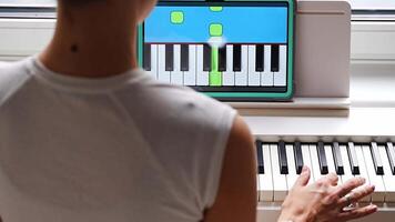 Back view of young woman learning to play the keyboard at home using an interactive app. Using mobile apps for self-study concept. video