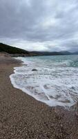 A stormy sea with crashing blue waves under dark clouds at the beach in Lustica Bay Montenegro. The powerful ocean swells and dramatic sky create a breathtaking display of natures force. video