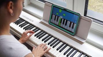 Close up view of young woman learning to play the keyboard at home using an interactive app. Using mobile apps for self-study concept. video