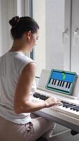 Close up view of young woman learning to play the keyboard at home using an interactive app. Using mobile apps for self-study concept. Vertical . video
