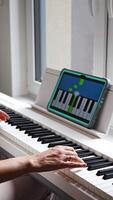 Hands playing a keyboard while following an interactive learning app on a tablet. Technology enables self-education in music without traditional lessons. Vertical . video