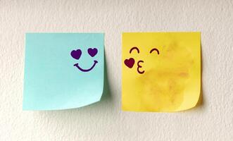 Couple in Love Concept. Two Sticky Notes on the white Wall with Cute Hand Drawn Emoticon Face as means of Love photo
