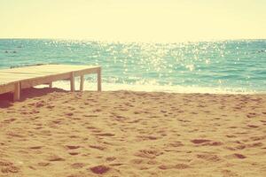 Serene Sunrise View of a Footbridge Leading to Tranquil Beach with Sparkling Waves photo