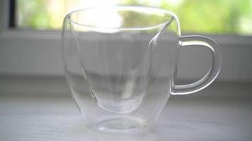 Transparent cup stands on windowsill and then hot ceylon tea is poured into it. Summer day outside window on background. Beverage for morning breakfast. video