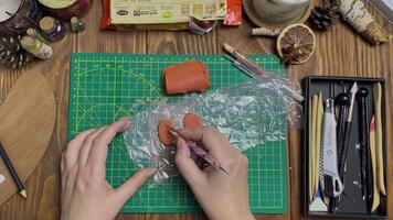 Female's hands draw face on clay with metallic stick. Tools for modeling and design of ceramic souvenirs on wooden table. Hobbies, handmade and crafts. video