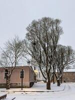 A quiet winter street scene featuring snow-covered trees, a small wooden house, and a distant church with blue domes. The cold atmosphere and evening light create a peaceful and nostalgic setting photo