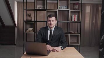 A focused businessman in a formal suit is giving a presentation at his desk using a laptop in a modern office setting video