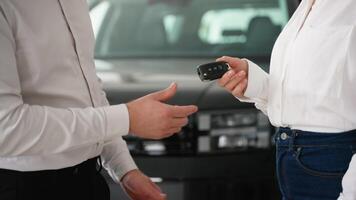 A car salesman hands over the keys to a new vehicle to a female customer in a dealership video