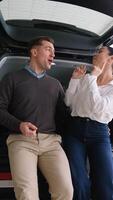 Happy couple dancing while sitting in new car trunk video