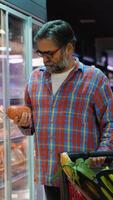 Senior man selecting sausage at grocery store refrigerated aisle video