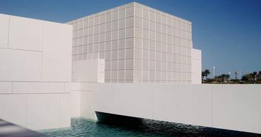 The facade of a modern minimalist white building of unusual architectural forms, surrounded by water. The Louvre Abu Dhabi video