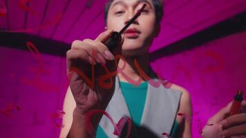 A young person writing on a glass surface with a red marker, surrounded by a vibrant pink background. The focus is on their expression and the colorful writing they create video