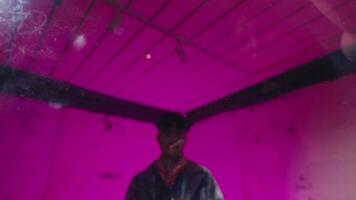 A young man wearing sunglasses and a jacket is writing with a marker on a glass surface. The background features vibrant pink lighting, creating a dynamic atmosphere video
