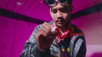 A young man wearing sunglasses and a leather jacket is writing with a marker on a glass surface. The background features vibrant pink lighting, creating a dynamic and artistic atmosphere video
