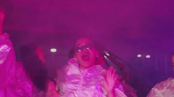une animé groupe de gens dansant dans une vibrant, coloré atmosphère avec néon lumières et brouillard. elles ou ils sont portant brillant, réfléchissant tenues, création une amusement et énergique vibe video
