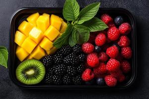 Fresh mango, kiwi, berries, and mint leaves arranged in black tray create vibrant and healthy snack. This colorful assortment is perfect for refreshing treat photo
