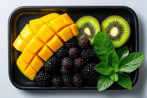 Fresh mango, kiwi, blackberries, and mint leaves arranged on black tray, creating vibrant and healthy fruit display. Perfect for refreshing snack or dessert photo