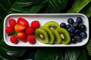 Fresh fruits including strawberries, raspberries, kiwi, and blueberries arranged on white tray, surrounded by green leaves, creating vibrant and healthy display photo