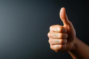 close up of hand giving thumbs up gesture, symbolizing approval and positivity against dark background. This conveys sense of encouragement and support photo