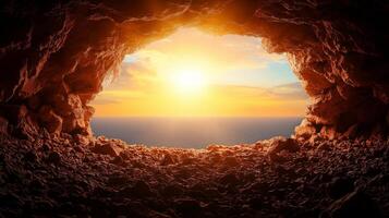 Cave entrance with rock formations, revealing stunning sunset over ocean. warm glow of sun illuminates cave, creating serene and tranquil atmosphere photo