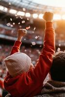 A father and son immerse themselves in the excitement of a lively football game, wearing matching jerseys and cheering joyfully as stadium lights shine in the golden hour photo