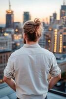 A modern man stands on a rooftop, gazing at the illuminated city skyline during dusk. The soft-focus, golden-hour lighting enhances the stylish atmosphere, with ample space for branding photo