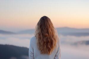 A woman gazes toward a blurred, misty horizon as the landscape gradually becomes clear. The soft glow of the golden sunrise envelops her, creating an inspiring moment of transition photo