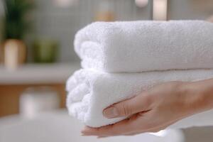 A close-up view highlights a cleaner's hands neatly folding fresh white towels, with a softly blurred bathroom backdrop exuding a warm and inviting spa ambiance photo