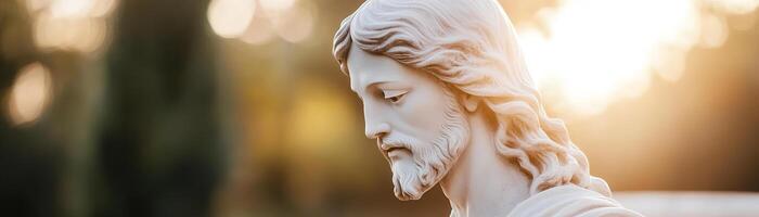 A detailed statue of Jesus with a serene expression is highlighted by warm sunlight filtering through trees, creating a peaceful, divine atmosphere photo