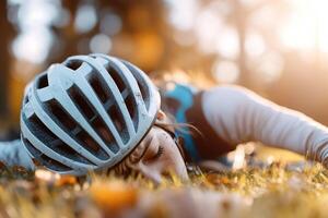A cyclist rests on their back after a fall, inspecting a scrape on their arm. Sunlight filters through the trees, creating a warm atmosphere in the grassy park photo