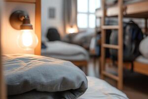 A shared dormitory features multiple bunk beds, warm soft lighting from a bedside lamp, and scattered backpacks, creating a cozy atmosphere perfect for travelers on a budget photo