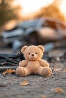 A small teddy bear lies on the pavement beside a wrecked vehicle. First responders tend to the scene, with a warm golden light creating an emotional atmosphere photo