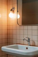 A cramped hostel bathroom with an old ceramic sink shows signs of wear. The rust-stained faucet and scratched mirror reflect the unique charm of urban exploration in a dim atmosphere photo