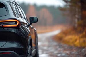 A sleek SUV is parked on a serene forest road, surrounded by vibrant autumn trees. The weather is overcast, creating a misty and tranquil environment perfect for an outdoor adventure photo