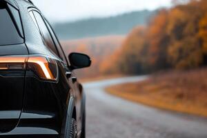 A black SUV is parked beside a winding road, with raindrops on its surface. Colorful autumn leaves surround the area, creating a serene and picturesque atmosphere photo