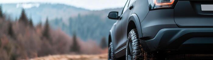 A matte-finished off-road vehicle stands on a rough path surrounded by a dense forest. The early morning light casts a soft glow on the wheels and landscape photo