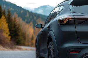 A sleek SUV is parked along a winding mountain road. The sun sets, casting a warm glow on the autumn-colored trees and distant mountains, creating a serene and picturesque setting photo