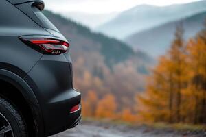 A modern SUV stands parked at a mountain viewpoint surrounded by vibrant autumn foliage. Misty hills create a serene backdrop, enhancing the sense of adventure photo