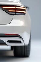 The rear view of a sophisticated white car showcases its sleek tail light design and polished exhaust tip in a clean studio environment. Perfect lighting enhances the modern features photo