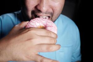 Man enjoying a pink frosted donut at a cozy setting photo