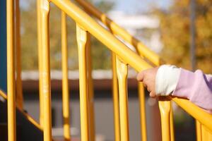 Child grasping yellow railing on playground stairs in autumn light photo