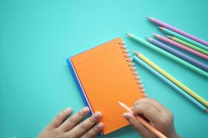 Child writing in a notebook with colorful pencils on a table photo