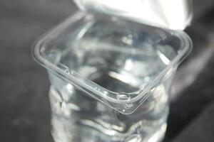 Clear container filled with water on a dark surface in daylight photo