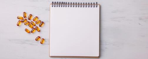 A blank notepad with a spiral binding sits on a light surface, accompanied by scattered golden capsules. photo
