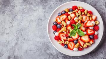 Plant-based ethics concept. A colorful bowl filled with strawberries, blueberries, raspberries, and nuts, garnished with fresh mint leaves on a textured gray surface. photo