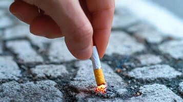 A hand is extinguishing a cigarette on a cobblestone surface, highlighting issues related to smoking and littering. photo