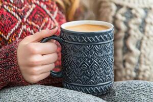 A cozy scene featuring a person holding a beautifully designed mug filled with coffee, surrounded by warm knitted fabrics. photo